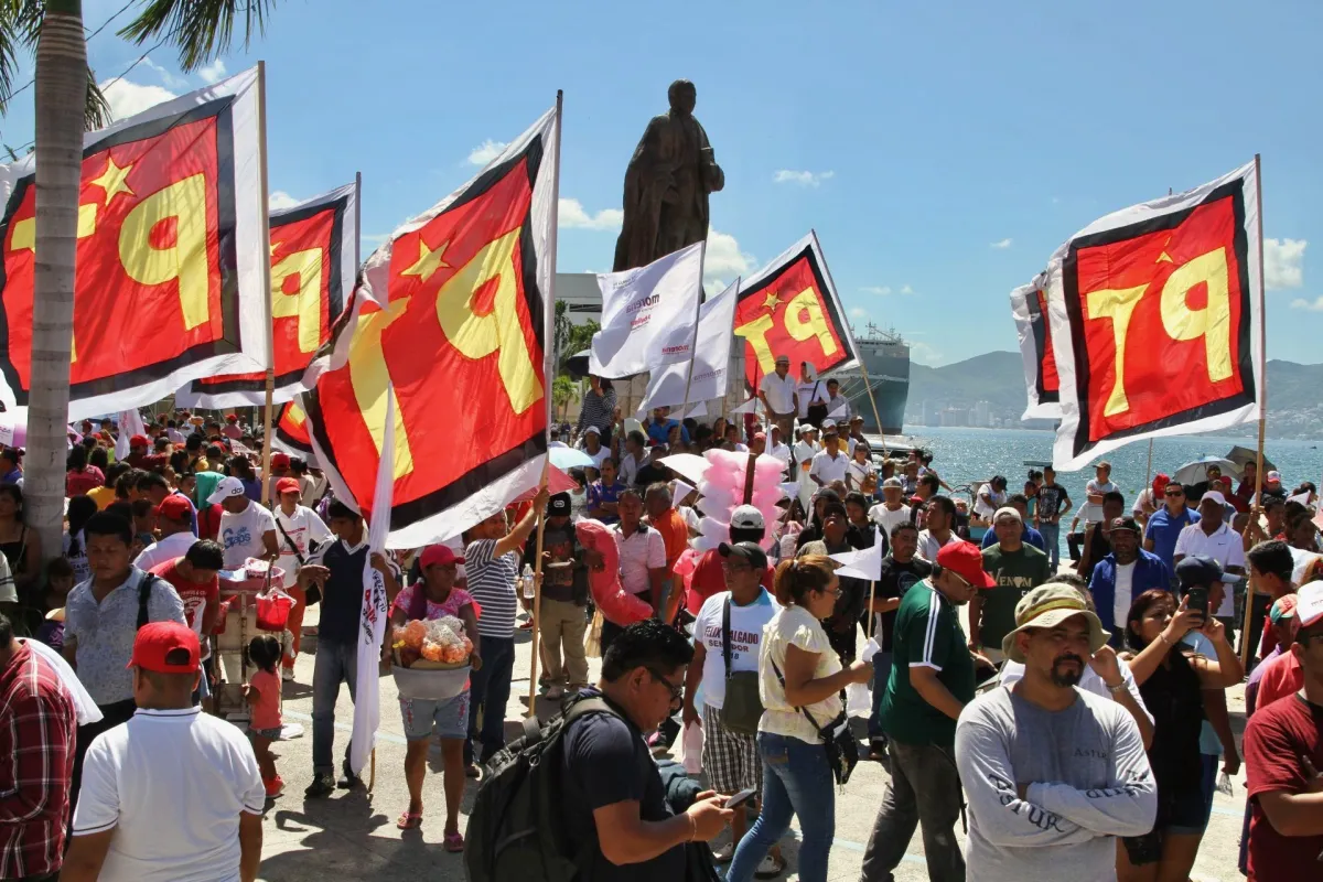 personas con banderas del PT con el mar de Acapulco de fondo