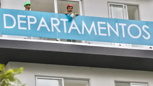 Dos trabajadores se asoman en un balcón de un edificio de departamentos en venta en CDMX.