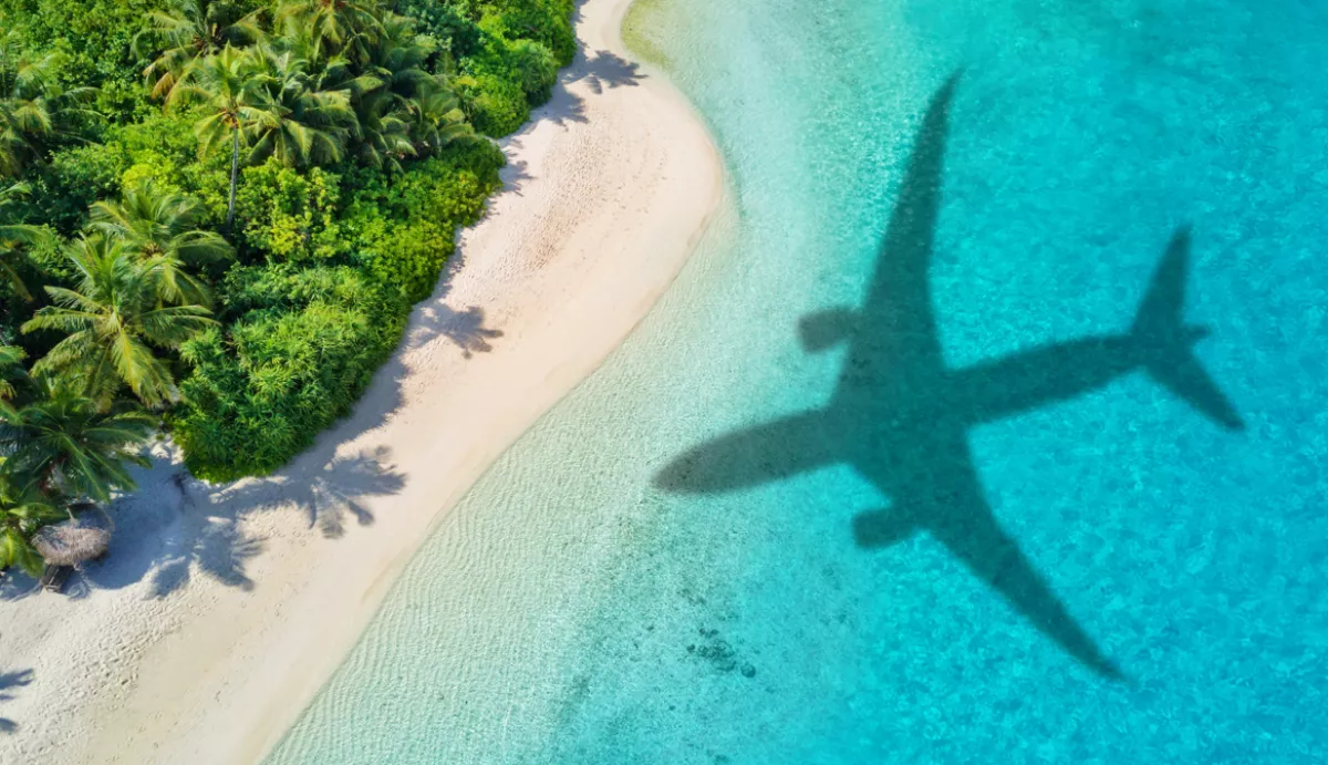 Sobre una playa de agua cristalina se ve la sombra de un avión.
