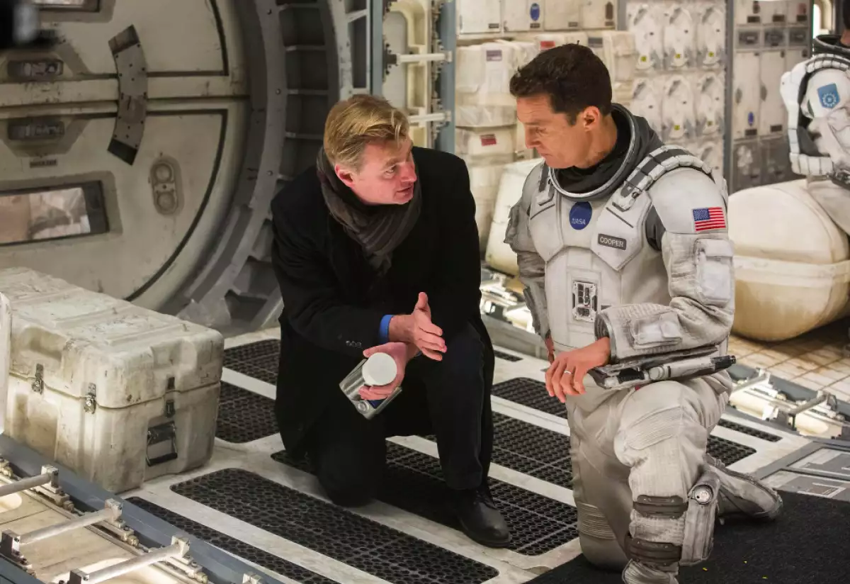 Foto de Christopher Nolan (a la izquierda vestido de negro) y Matthew McConaughey (a la derecha con un uniforme de astronauta) ambos hincados en el set de grabación de la película Interstellar.