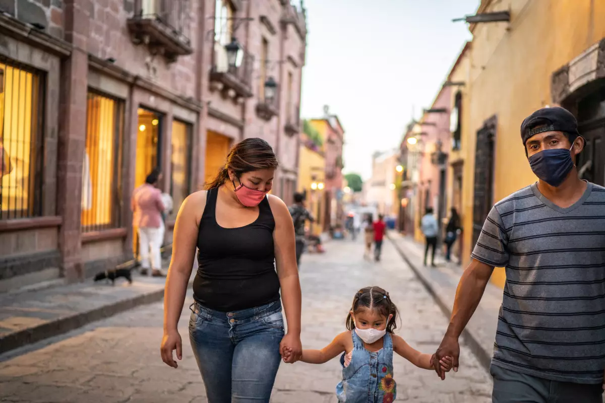 Una familia mexicana camina por la calle con cubrebocas. 
