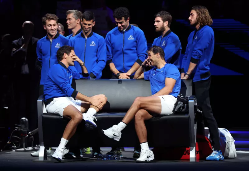 Foto de Rafael Nadal y Roger Federer sentados en una banca despidiéndose uno del otro. Federer se cubre el rostro para limpiarse las lágrimas y Nadal lo ve sonriendo.