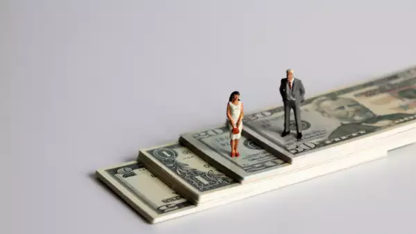 A miniature man and a miniature woman standing on a pile of bills.