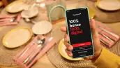 pantalla de un smartphone que muestra la app de Openbank, mientras una mano sostiene el teléfono por encima de una mesa con los cubiertos bien ordenados en un restaurante