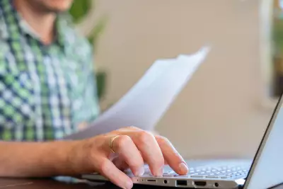 Closeup Of Hand Typing On Laptop Keyboard Holding Paper Documents Remote Work