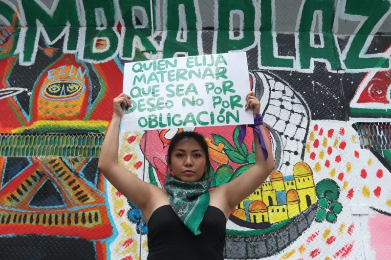 Una mujer joven muestra un cartel con la leyenda "quien elija maternar, que sea por deseo, no por obligación".