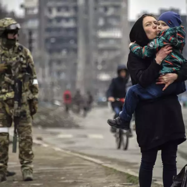 Una mujer sostiene y besa a un niño junto a soldados rusos en una calle de Mariupol el 12 de abril de 2022, mientras las tropas rusas intensifican una campaña para tomar la ciudad portuaria estratégica.