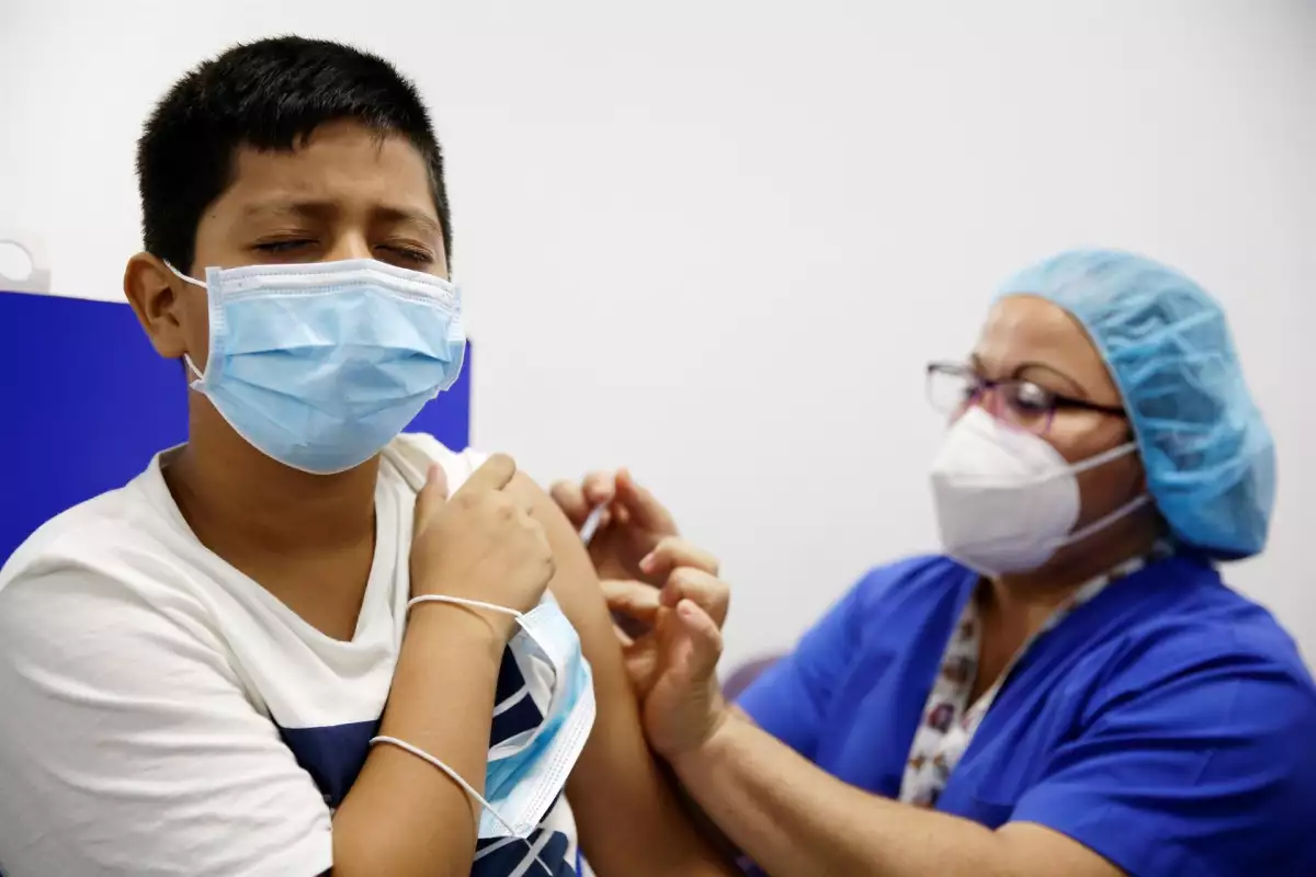 Estas son las fechas y las sedes para que los niños reciban la vacuna covid en CDMX. (Mujer del personal de salud vacunando a un niño contra covid).