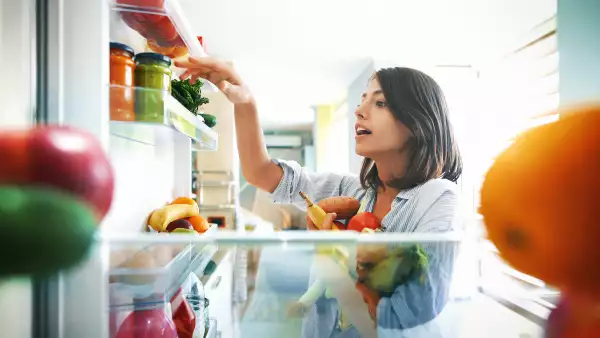 Woman picking up some fruits and veggies from the fridge