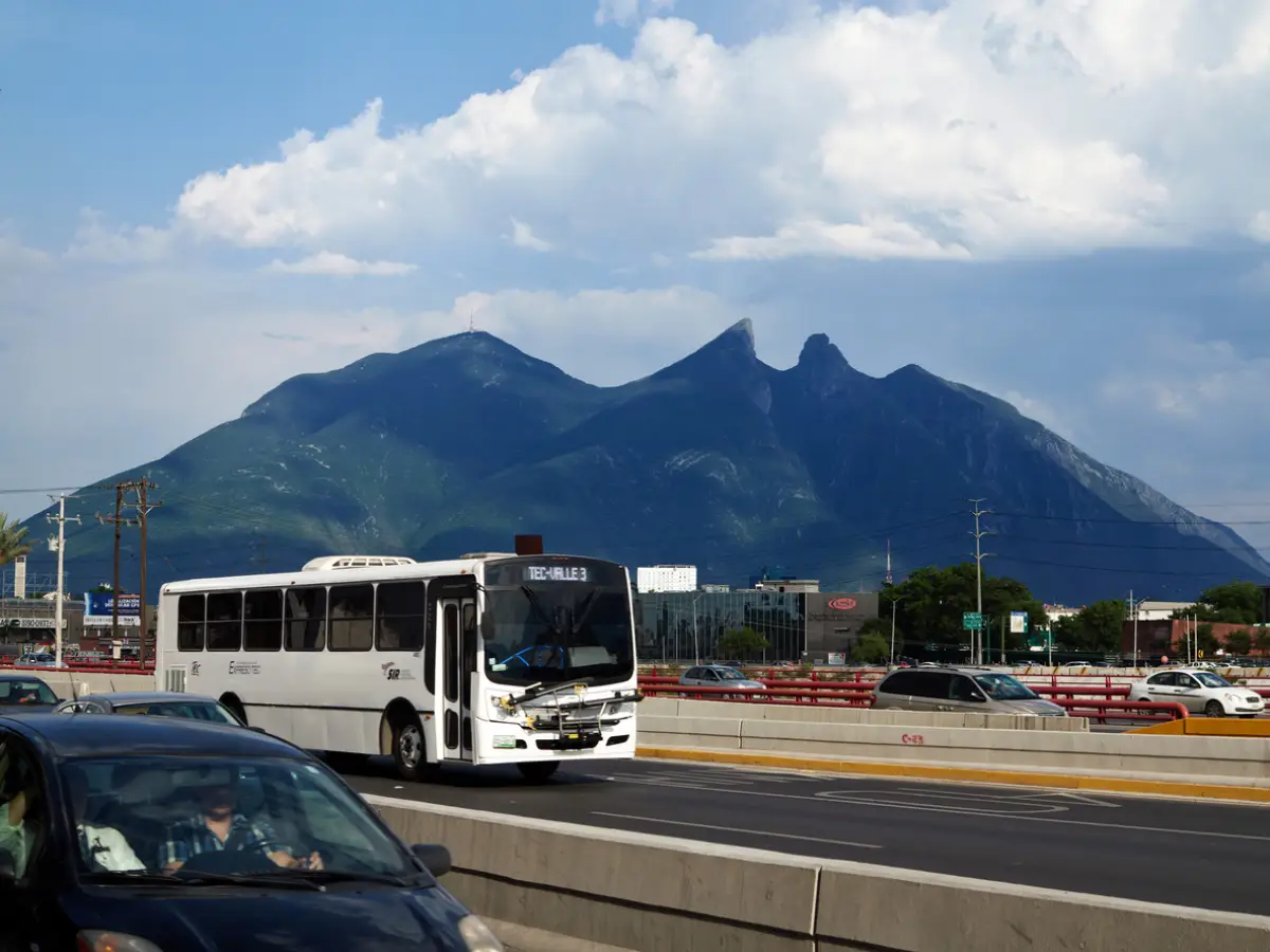 autos y autobus en una vialidad de Monterrey con el cerro de la silla al fondo.
