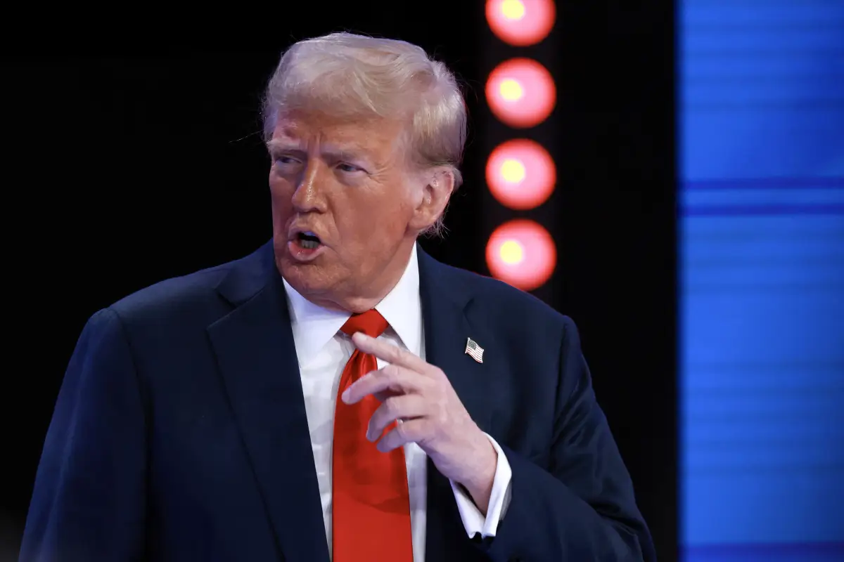 Donald Trump, un hombre blanco de 78 años asiste a un evento para votantes latinos indecisos. Lleva puesto un traje azul, camisa blanca y una corbata roja con un pin de la banera estadounidense en el lado izquiero del saco. 