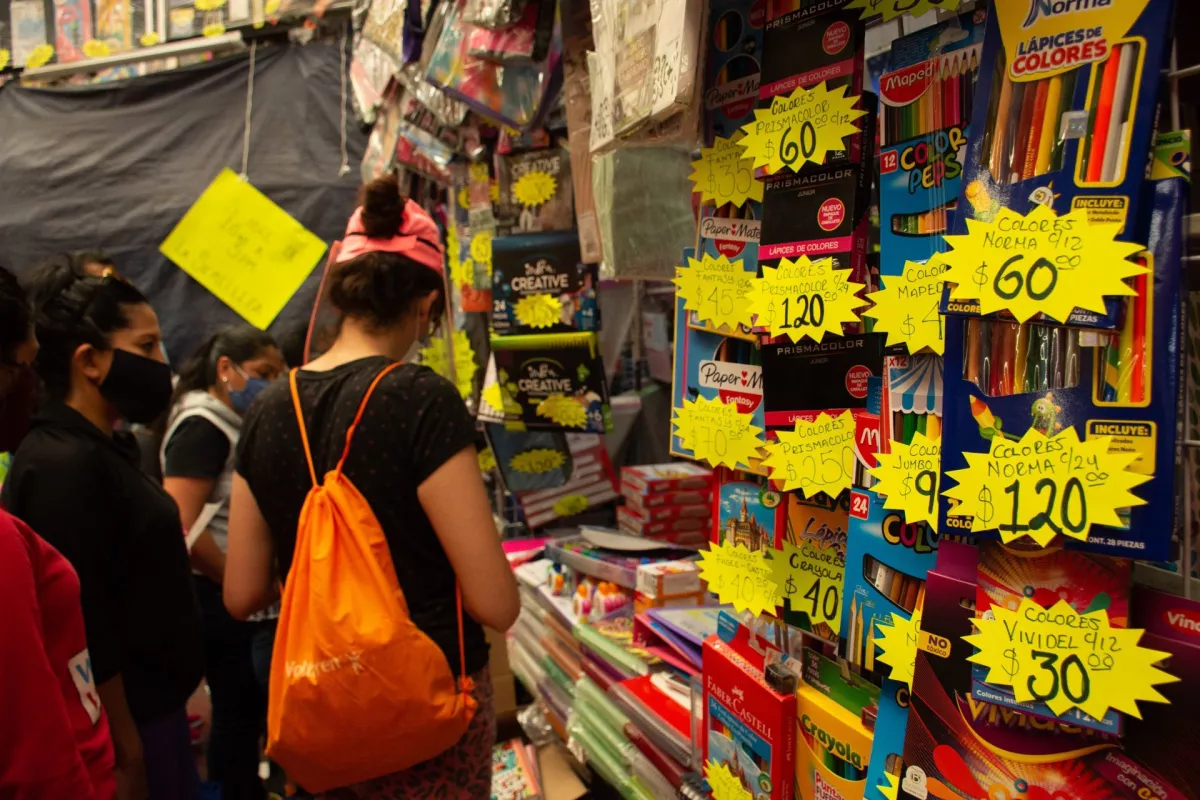 Una mujer compra cuadernos en un puesto. Este es el precio de la lista de útiles escolares. 