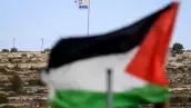 Esta foto tomada desde la aldea de Umm Safa, al norte de Ramallah en la Cisjordania ocupada, muestra una bandera palestina (en primer plano) y una bandera israelí ondeando en la cima de una colina con vistas al pueblo el 16 de febrero de 2026. El gobierno de Israel ha aprobado un proceso para registrar la tierra en Cisjordania como "propiedad estatal", lo que provocó la condena de las naciones árabes y los críticos que dijeron que aceleraría la anexión del territorio palestino.