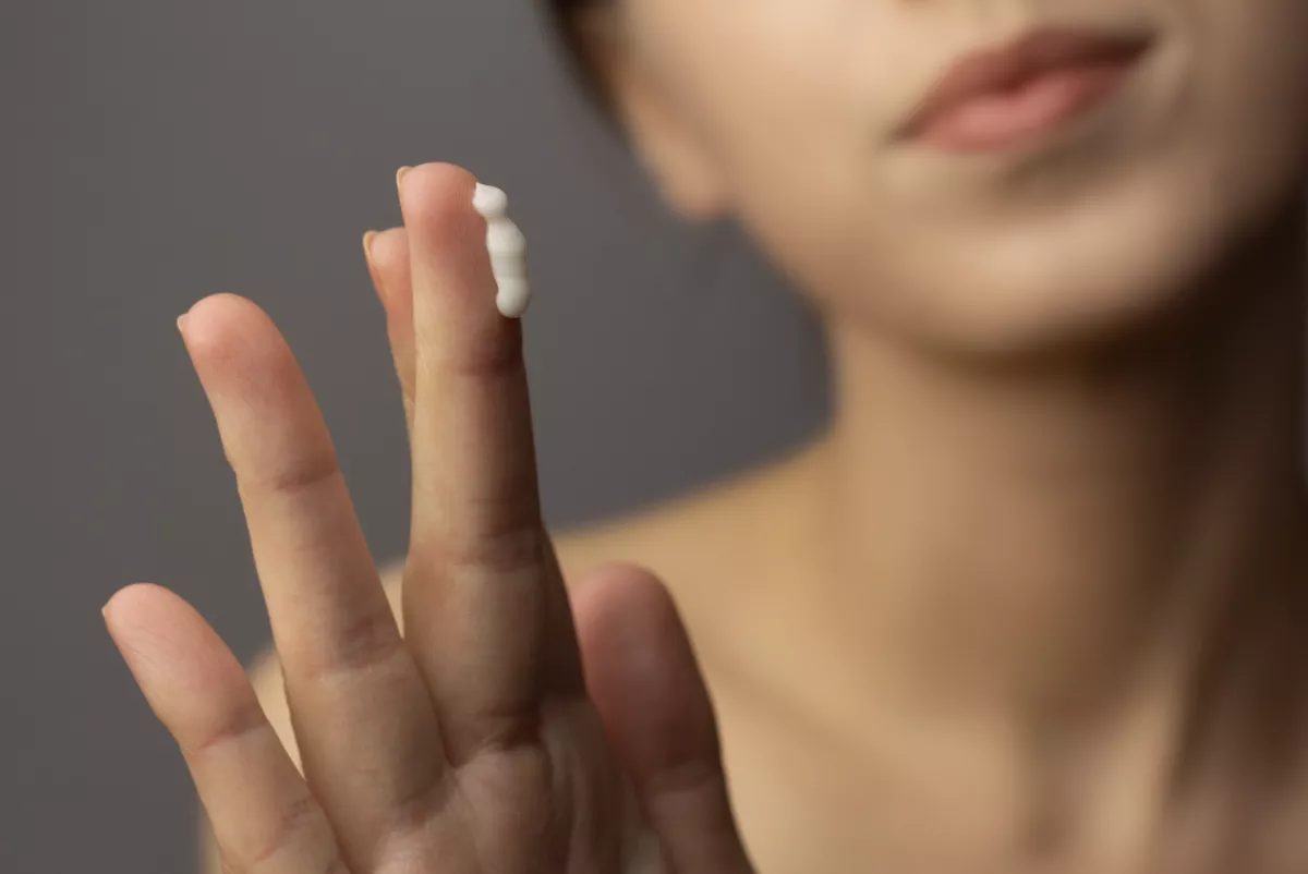 una mujer muestra que en sus dedos tiene un producto de belleza para su rostro, como isdin