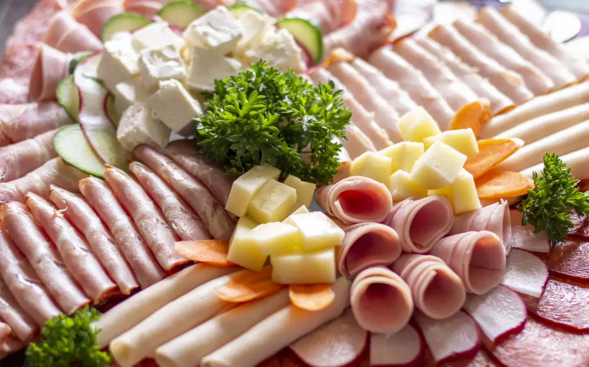 large appetizer plate filled with slices of meat, bacon, salami, cheese, cherry tomatoes, olives