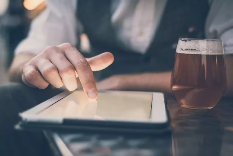 Hombre usando una tablet con un vaso de cerveza junto a él
