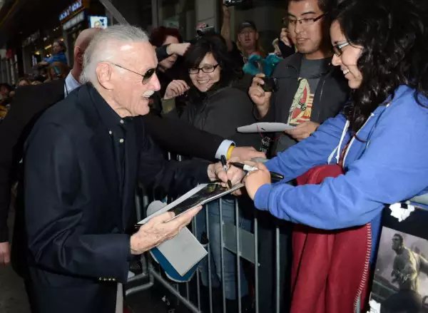 Foto de Stan Lee vestido de negro firmando autógrafos a fans