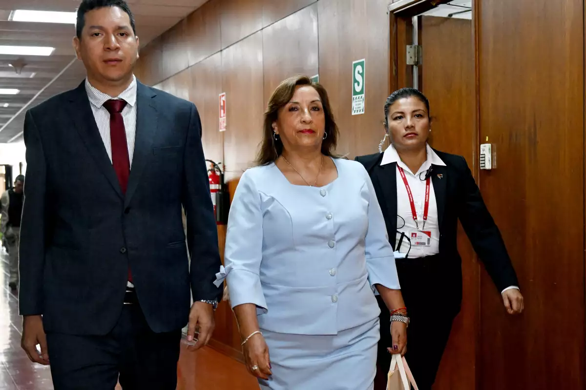 La presidenta de Perú, Dina Boluarte, llega a la oficia de la Fiscal en Lima, Perú. Está escoltada por dos personas. Viste un traje color celeste y sonríe. 