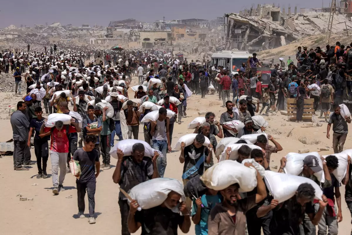 La gente camina con sacos de harina entregados después de que camiones que transportaban ayuda humanitaria entraran en el norte de Gaza el 27 de julio de 2025 desde el cruce fronterizo de Zikim.
