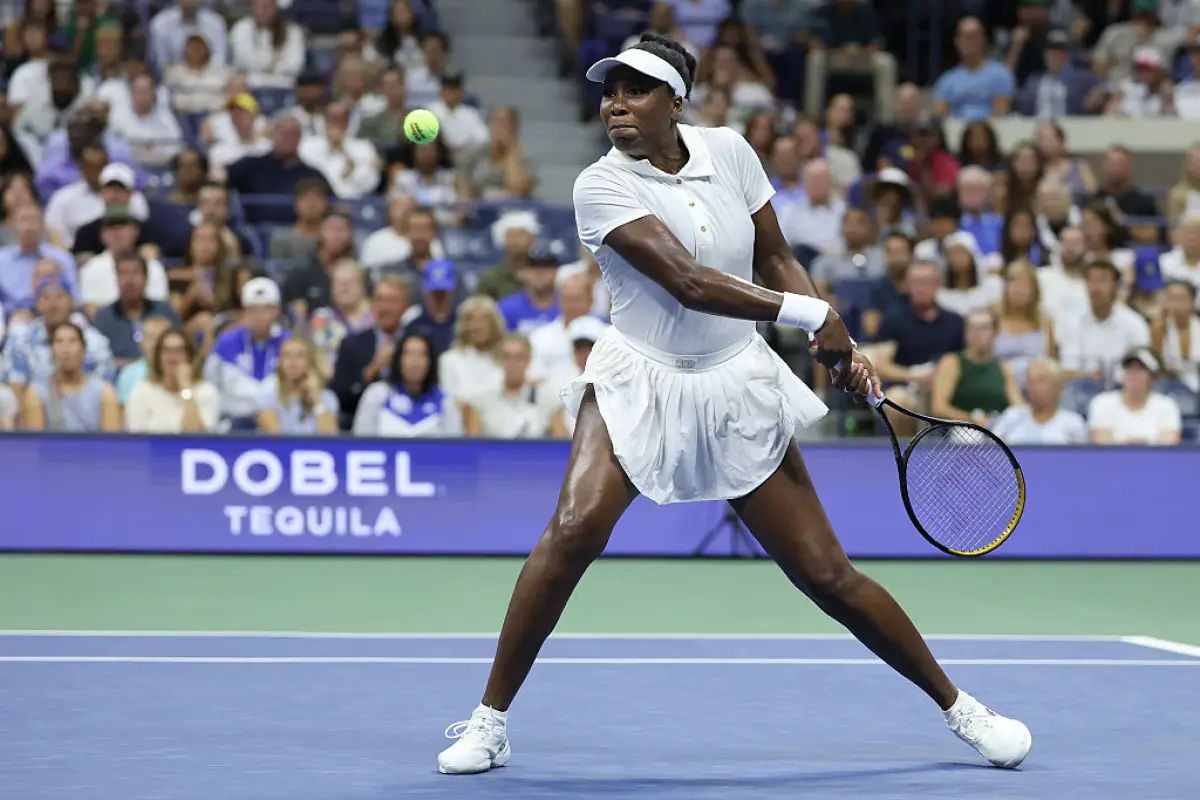 Foto de Venus Williams con uniforme de tenis totalmente blanco a punto de golpear con la raqueta la pelota.