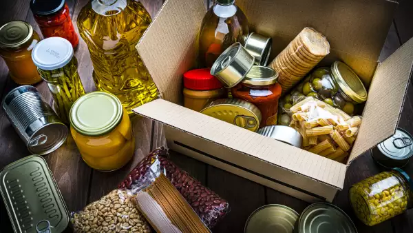 Cardboard box filled with non-perishable foods on wooden table. High angle view.