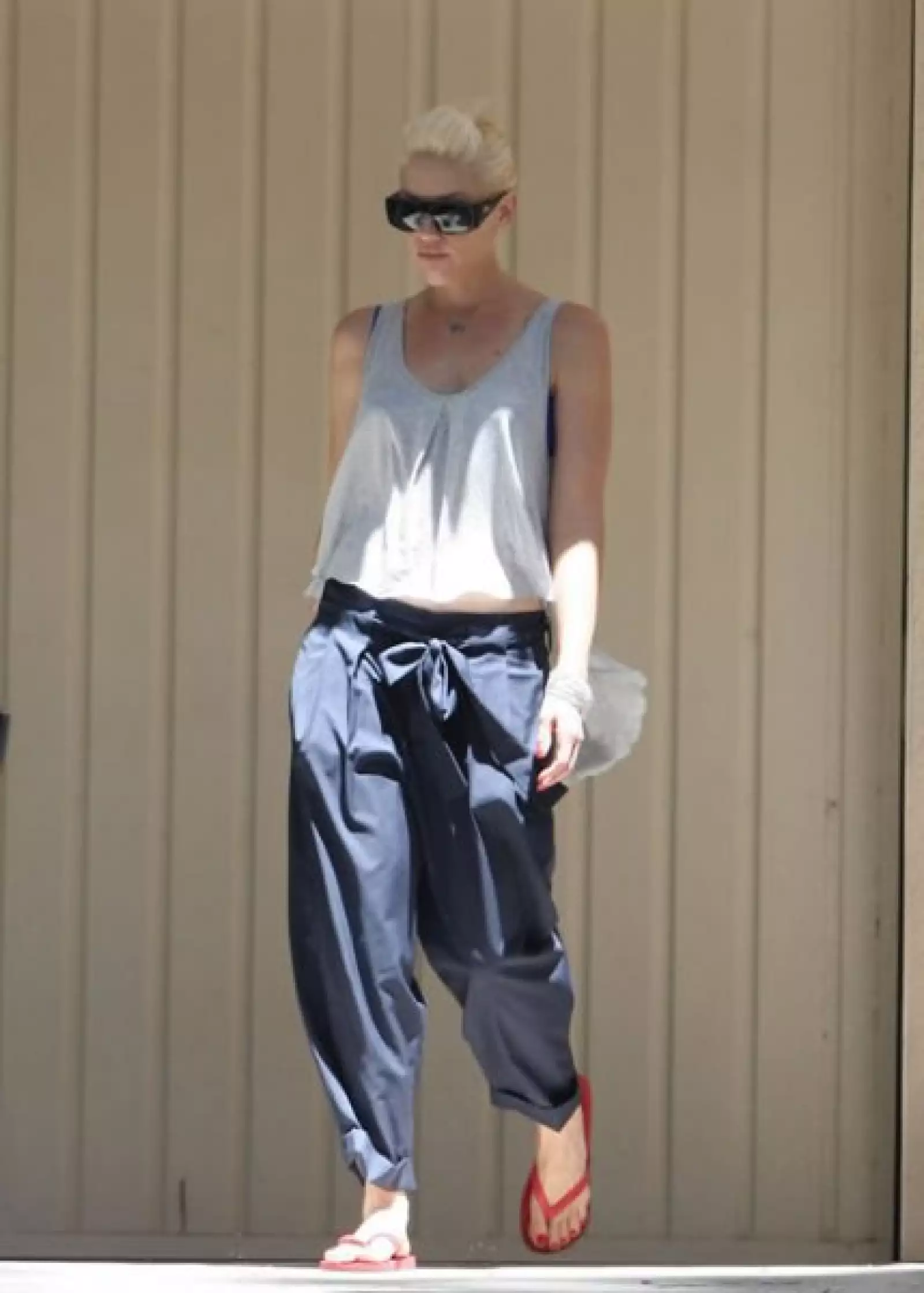 Gwen stefani, siempre a la mda, usa unos pantalones harem con moño, top gris y flip flops rojas.