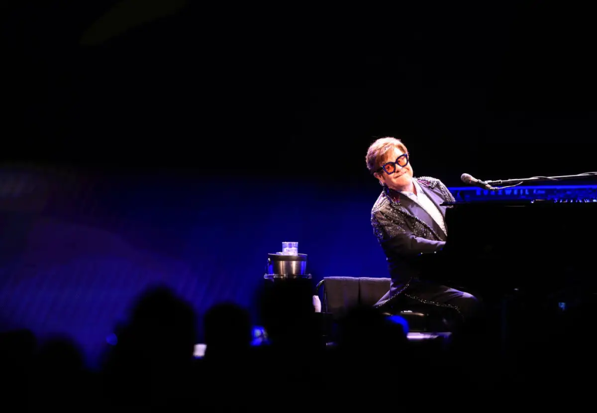 Foto de Elton John sentado frente a su piano durante un concierto y sonriendo al público.
