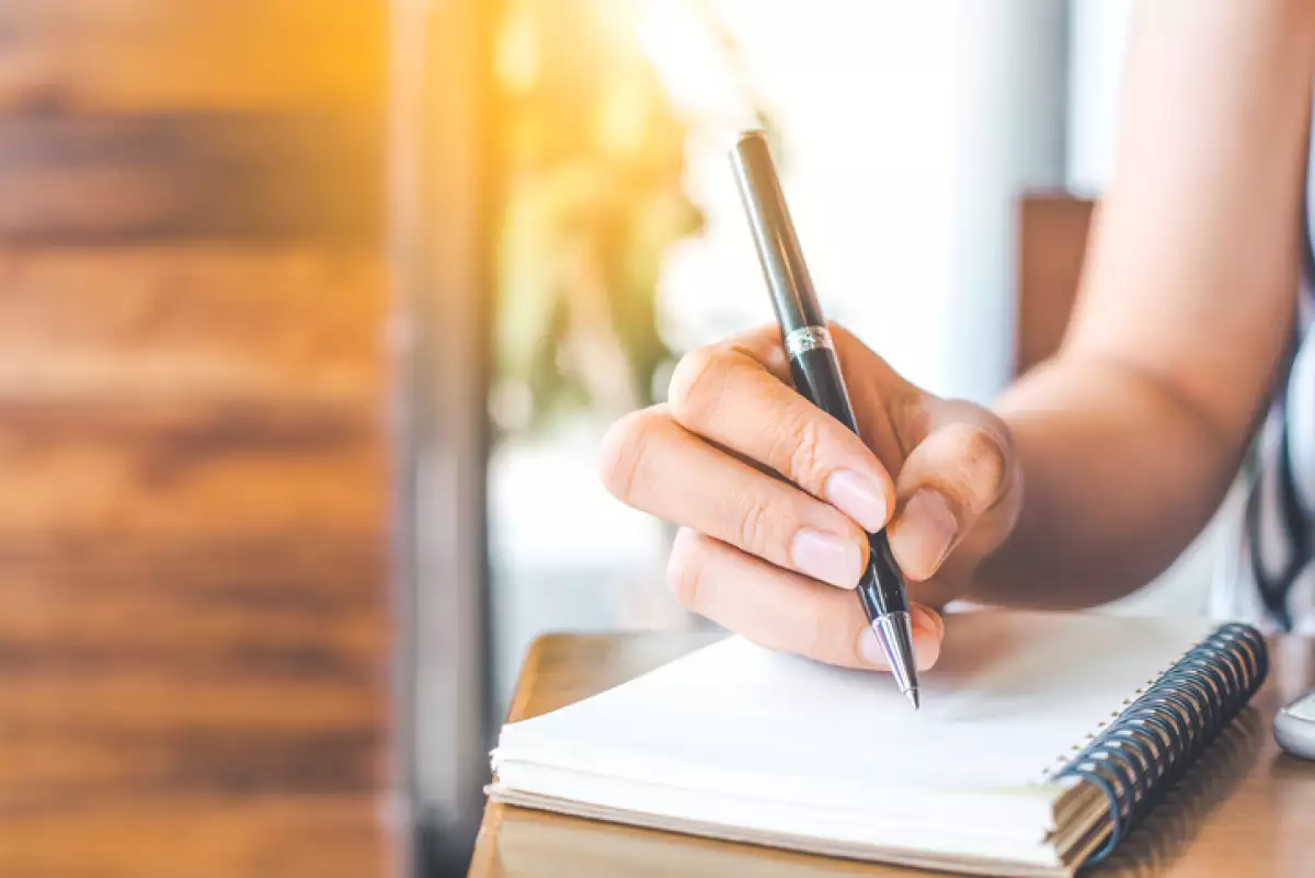 woman's hand is writing on a blank notepad with a pen
