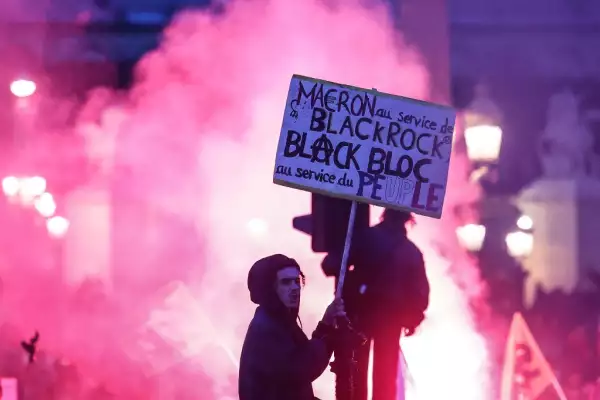 Un manifestante en un semáforo sostiene un cartel que dice "Macron al servicio de Black Rock, Black block al servicio del pueblo" durante una manifestación en la Place de la Concorde después de que el gobierno francés impulsara una reforma de las pensiones en el parlamento sin votación. utilizando el artículo 49,3 de la constitución, en París el 16 de marzo de 2023.