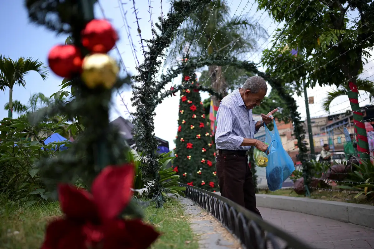 Un hombre revisa una bolsa de plástico con comida frente a las decoraciones navideñas en una plaza pública, mientras comienza la temporada navideña según un decreto del presidente de Venezuela, Nicolás Maduro, en Caracas, Venezuela, el 1 de octubre de 2024.