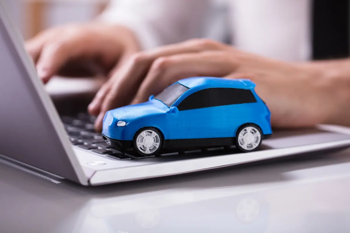 Un vehículo azul a escala representa la contratación de un seguro para auto en línea al estar encima de una laptop 