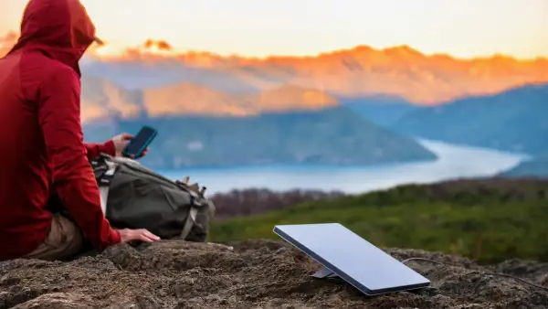 Una persona en medio de una montaña buscando internet con una antena de Starlink.