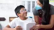 El 15 de mayo se celebra el Día del maestro en México. (Alumno con careta y profesora con cubrebocas).