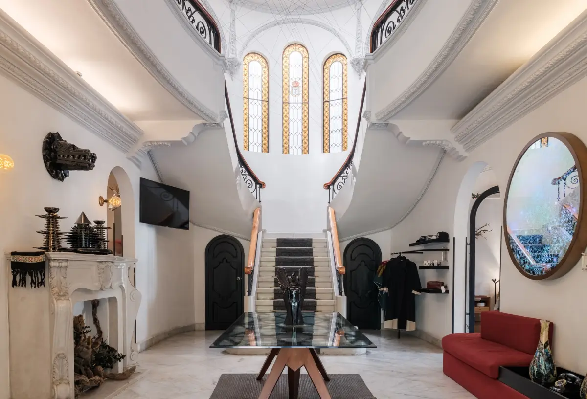 Interior del Pug Seal Allan Poe se observa el lobby con una escalera central que se abre en dos, hay un espejo, un sillón, chimenea y piezas decorativas con motivos de la cultura mexicana.