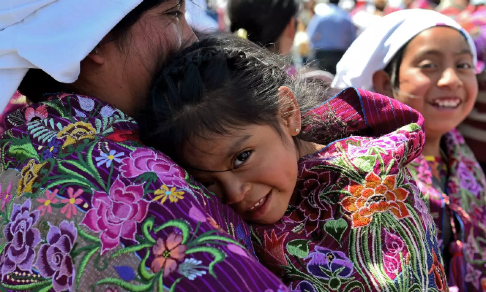 Una pequeña se refugia del sol en los brazos de su madre.