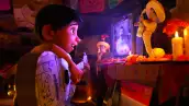 Foto de una escena de la película animada de Pixar, Coco, con el pequeño Miguel tocando su guitarra viendo emocionado la televisión.