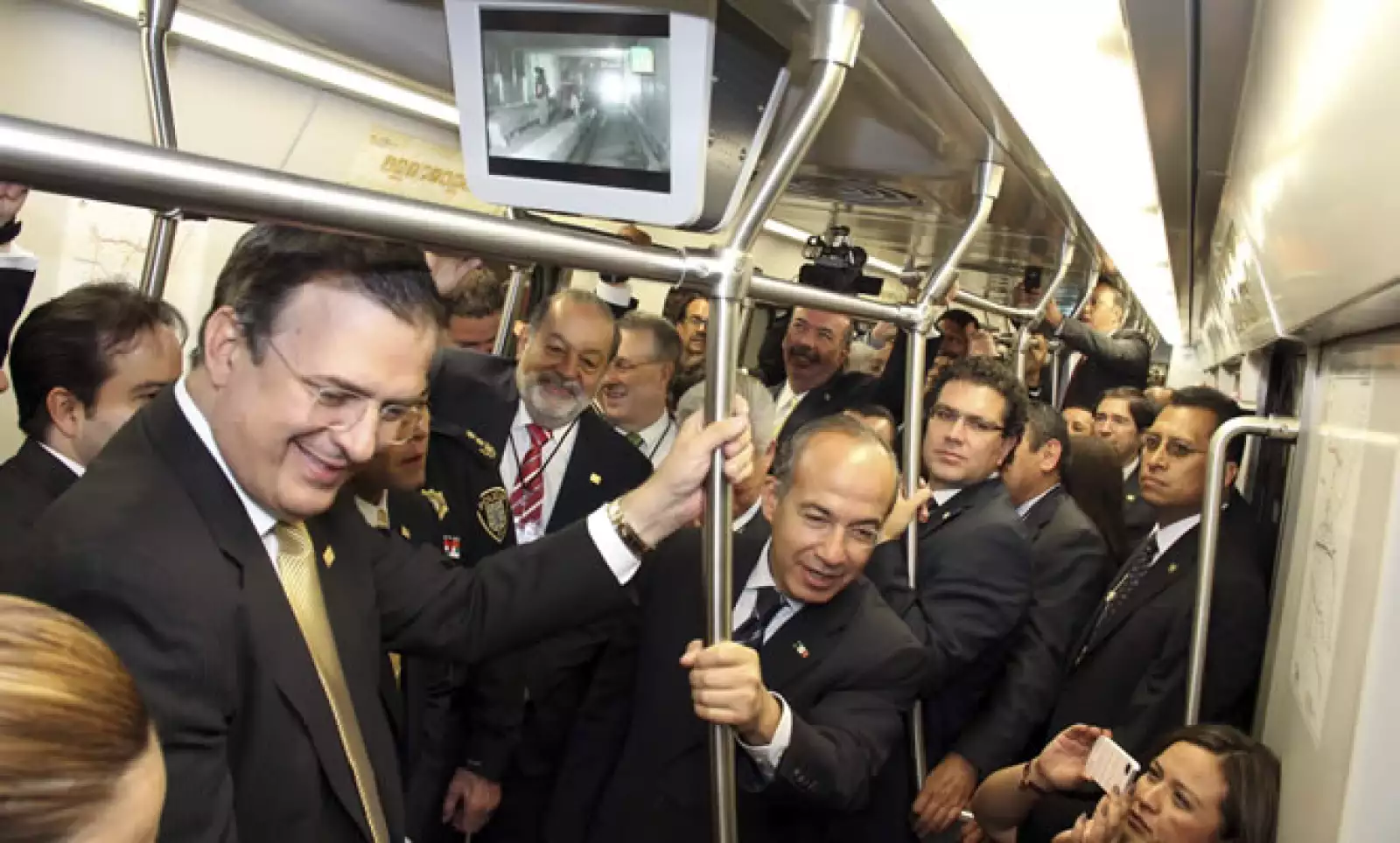Marcelo Ebrard (izq), Carlos Slim (centro al fondo), y Felipe Calderón (der), sonrientes durante el viaje en metro de inauguración.