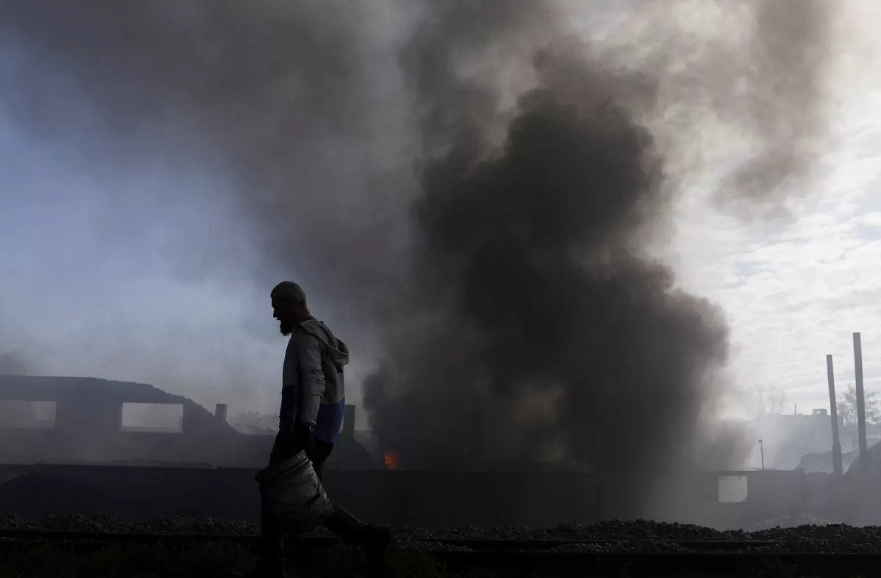 (Una persona lleva baldes mientras trabaja para extinguir un incendio en una planta en llamas, luego del bombardeo ruso en medio del ataque de Rusia a Ucrania, en Jarkov, Ucrania)