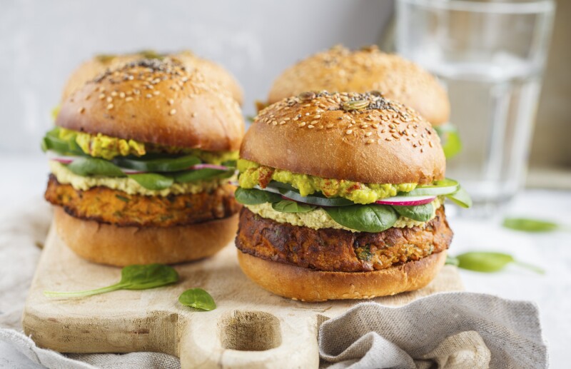 Healthy baked sweet potato burger with whole grain bun, guacamole, vegan mayonnaise and vegetables on a wooden board. Vegetarian food concept, light background.