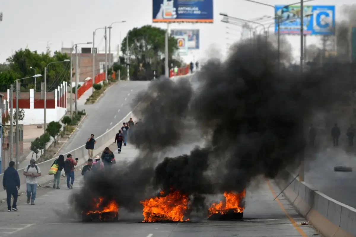 La gente camina junto a los neumáticos quemados puestos por los manifestantes para bloquear el puente San Isidro, en la entrada a Arequipa, Perú, durante las protestas para pedir la renuncia de la presidenta Dina Boluarte, el 19 de enero de 2023