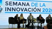 Dos hombres de traje y tres mujeres con vestidos formales frente una mesa de centro. Un letrero con Semana de la Innovación.jpg