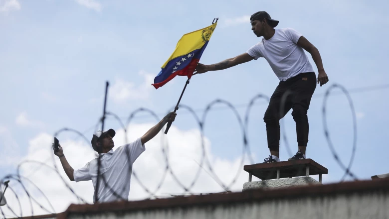 A man gives a flag of Venezuela to one another, on the roof of the Consulate of Venezuela, during a protest in Bogota