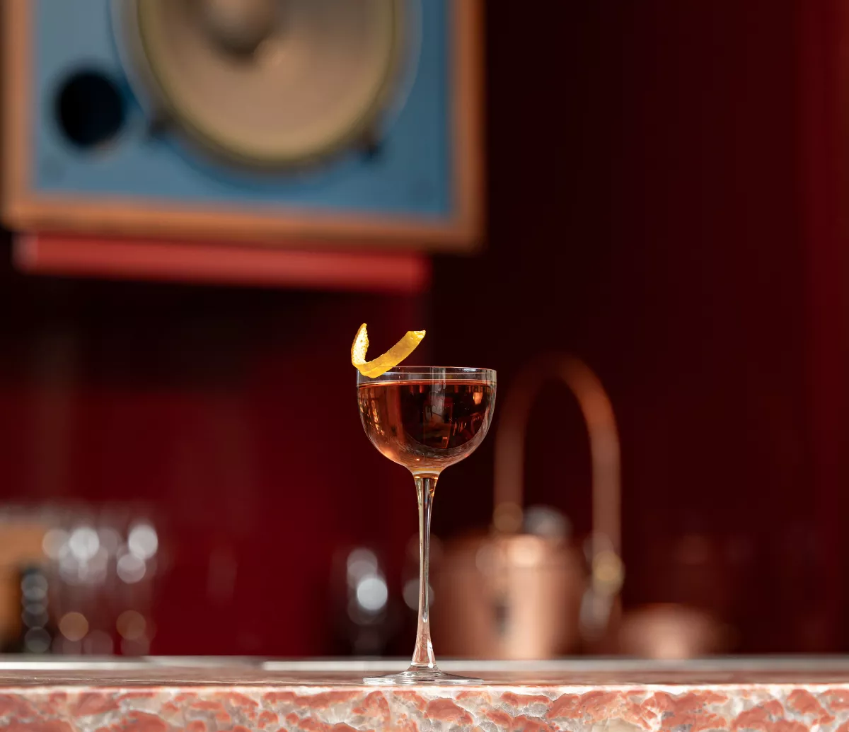Foto de una copa de coctelería en primer plano y al fondo una bocina del listening bar SHHH, en CDMX.