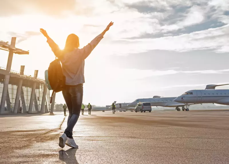 imagen de joven levantando los brazos para celebrar que está por abordar el avión que la lleva a sus próximas vacaciones de verano.