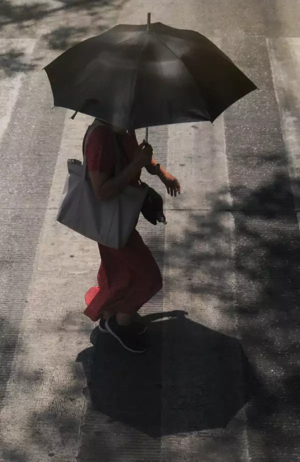 Una mujer cruza la calle protegiendose del sol con una sombrilla.
