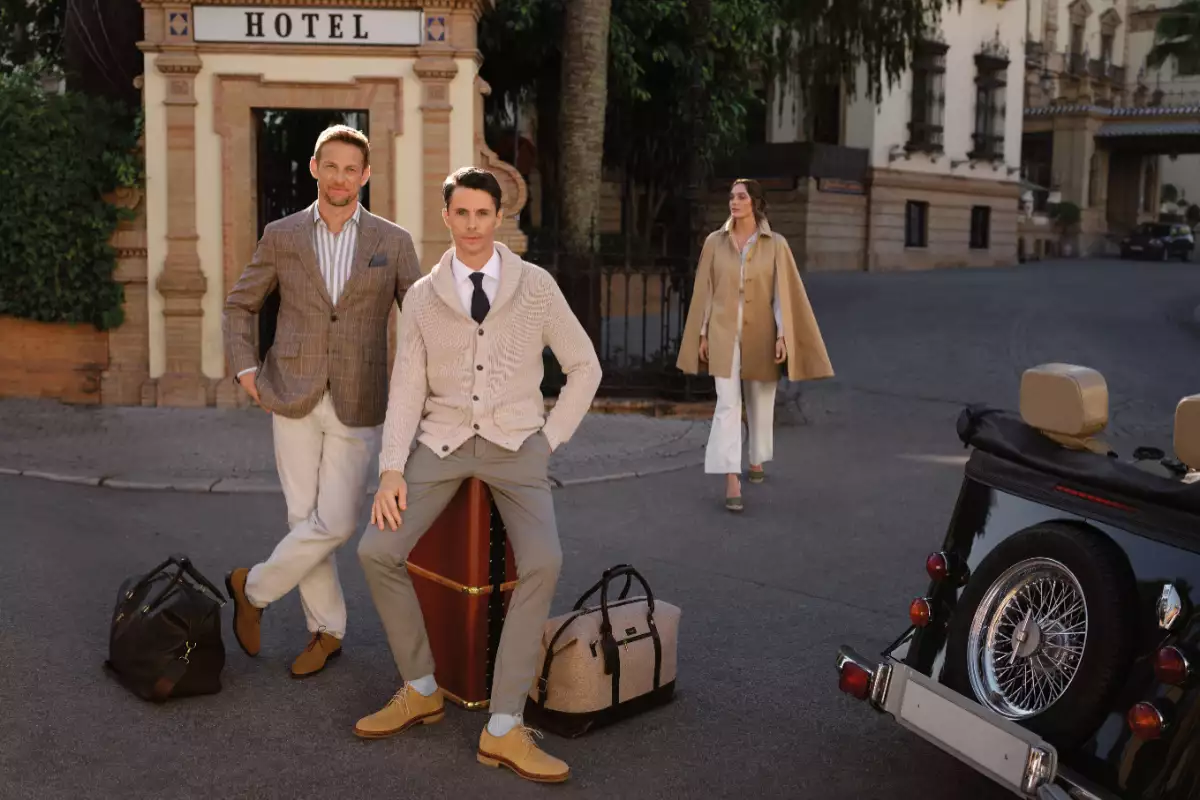 Foto de Matthew Goode sentado sobre un baúl de viaje acompañado del expiloto de F1 Jenson Button.