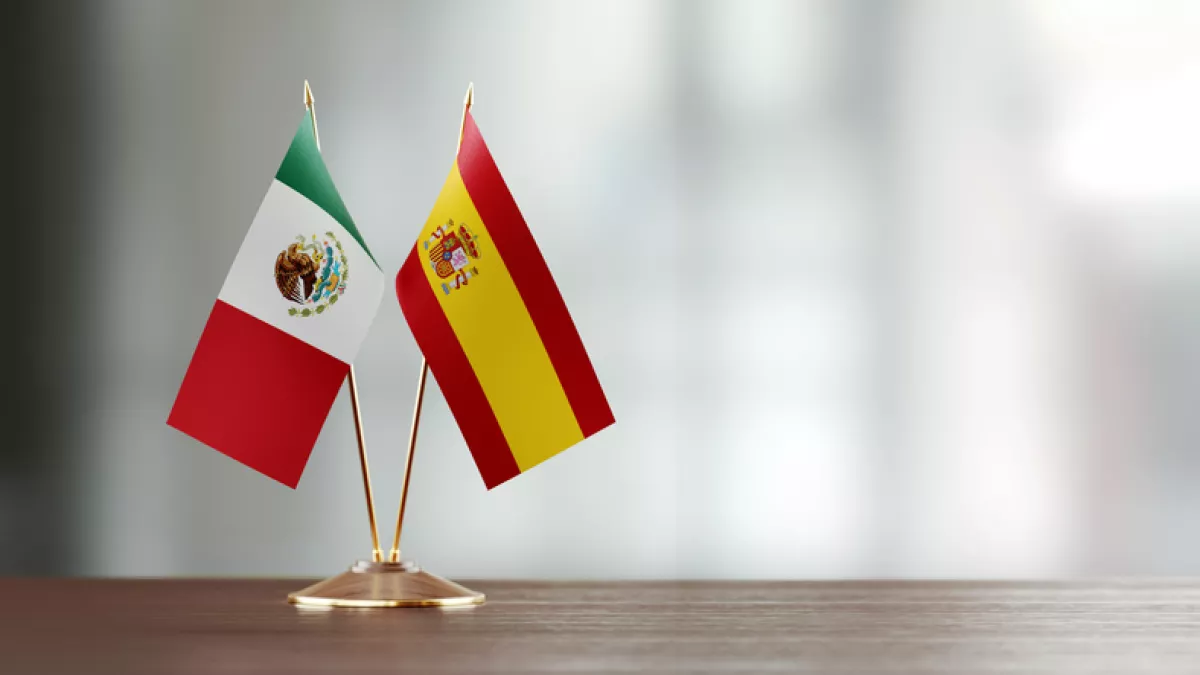 Spanish And Mexican Flag Pair On A Desk Over Defocused Background