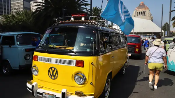 Combi amarilla con bandera de VW transita frente al Monumento a la Revolución.