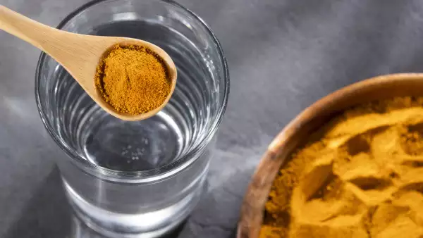 Spoon with organic turmeric and glass of filtered water