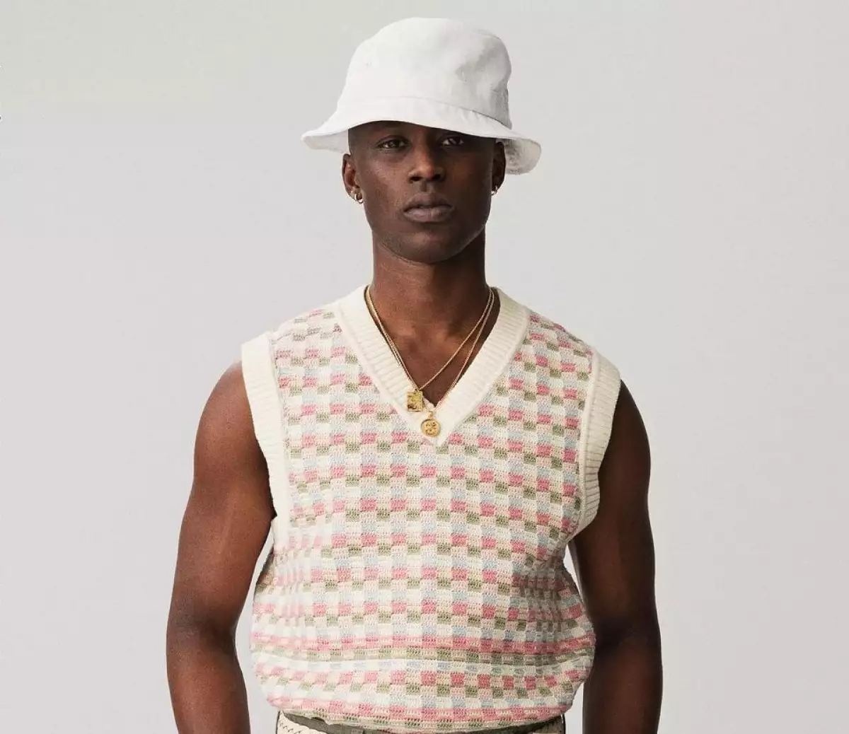 Foto de un modelo vistiendo un chaleco de punto y un gorro blanco de la marca Aimé Leon Dore.